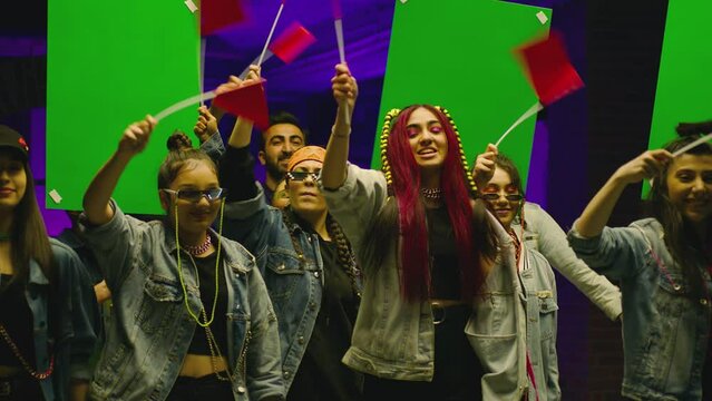 Group of stylish positive young people or students protesting , shouting , jumping . Boys and girls holding red flags , green screen posters . Peaceful , colorful meeting . Rally concept slow motion
