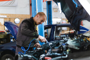 Handsome mechanic in uniform is working in auto service garage. Repair service.