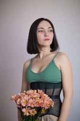 brunette girl in a black corset holding chrysanthemums in her hands