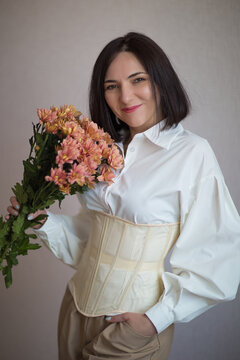  girl in a white shirt and beige corset holds flowers in her hands