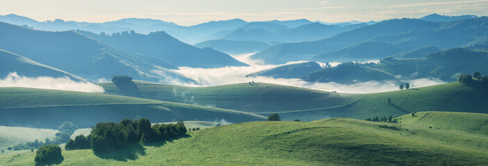 Mountains and hills in morning light, fog in the valley, panoramic view