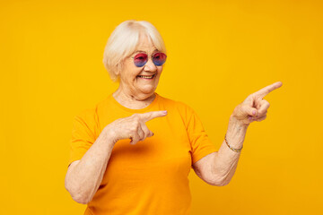 Portrait of an old friendly woman in casual t-shirt sunglasses yellow background