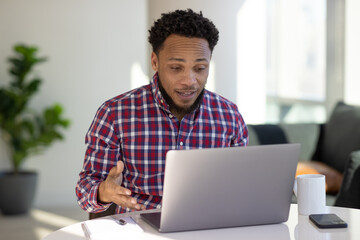 Black man at home remote working on laptop computer talking with colleague