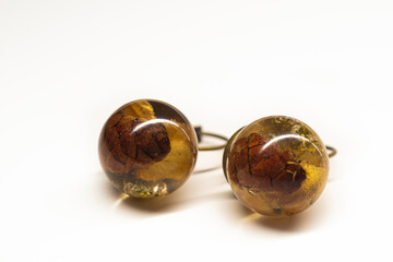 Sphere resin ball earrings closeup. Natural dried plants inside handmade jewelry. Smooth surface, brass base. Selective focus on the details, object isolated on white background.