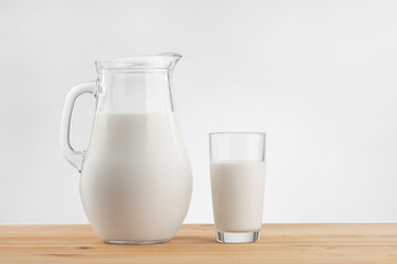 a glass jug with milk and a glass stand on a wooden table with a linen tablecloth