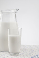 a glass jug with milk and a glass stand on a wooden table with a linen tablecloth