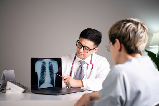 Asian medical doctor orthopaedic surgeon wearing stethoscope showing x-ray image from laptop while explaining and soothing patient about diagnosis and treatment plan in examination room in hospital. 