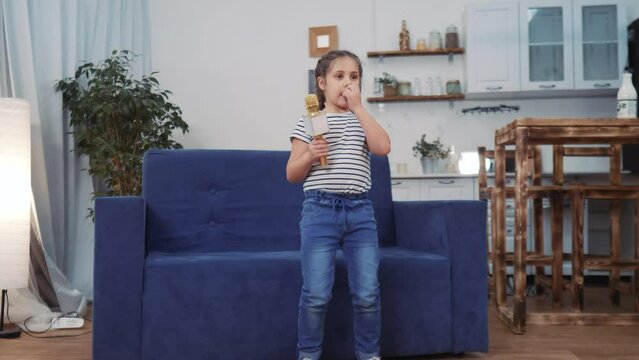 little child daughter a sing dancing at home. stay home active leisure happy childhood concept. child daughter dancing sing dream next to the sofa with a microphone. kid dream dance