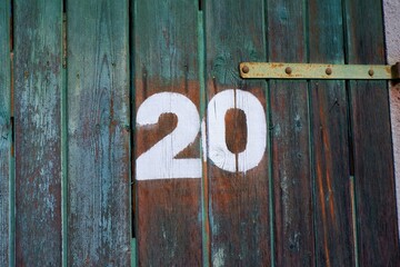 White colour number twenty on an old abandoned weathered painted natural wooden gate of a garage in...