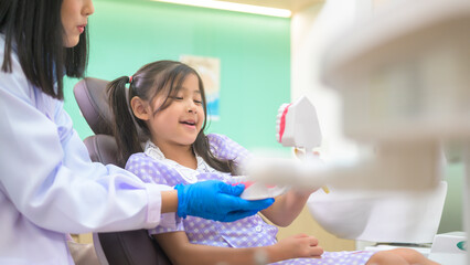 Female dentist demonstrating how to brush teeth to a little girl in dental clinic, teeth check-up and Healthy teeth concept