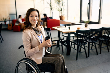 Happy entrepreneur in wheelchair enjoys in her coffee break in office and looks at camera. - obrazy, fototapety, plakaty