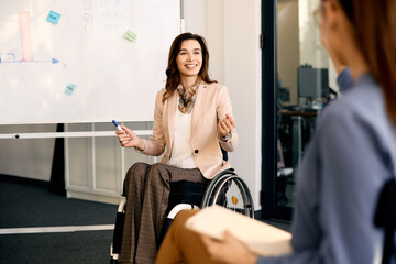 Happy entrepreneur in wheelchair explains inclusive business strategy to her coworkers during presentation in meeting room.