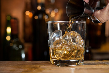 whisky pouring from jigger into glass of ice 