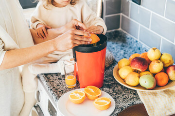 Little baby girl with mother makes freshly orange juice.