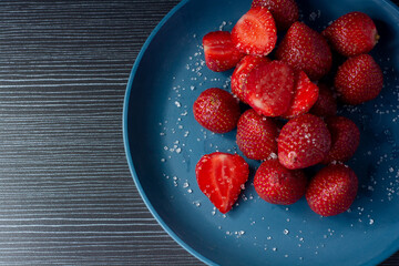 Strawberries on a plate with dark background. Strawberries on a plate with a sprinkle of sugar.