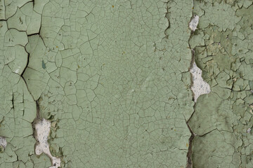 Green peeling paint on the wall. Old concrete wall with cracked flaking paint. Weathered rough painted surface with patterns of cracks and peeling. High resolution texture for background and design.