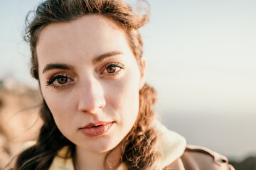 Closeup portrait of sensual young brunette woman in red dress, happily dancing outdoors isolated on blurry sea background with natural bokeh in soft warm sunset backlight. Selective focus.