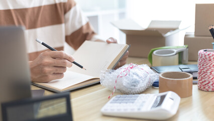 Fototapeta premium Young man uses a laptop to chat with customers who come to order product, Working at home and owning businesses, Online shopping SME entrepreneur, packing box, Sell online, freelance working.