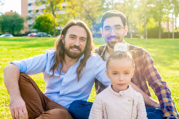 A gay male couple with their daughter sitting on grass