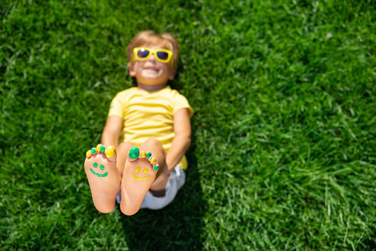 Happy child with smile on feet lying on green spring grass