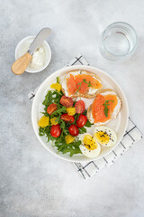 salad with tomatoes, two salmon sandwiches, boiled egg on the white plate and glass of water