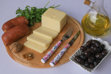 Various types of cheese on a wooden board. Olive oil, parsley, walnuts and olives in glass bottle...