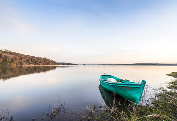Obraz premium A bright green boat at the shore of a quiet Lake on a sunny day.
