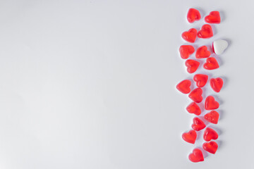 Row of red jelly candies in hearts form with one white heart, isolated on white background on the right side. Top view.