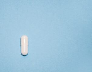 One single tablet or capsule lie on a light blue background with space for text. Pharmaceutical, Covid-19 or coronavirus