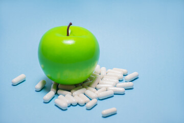 A green apple lies on white capsules or tablets on a blue background with a place for the text:...