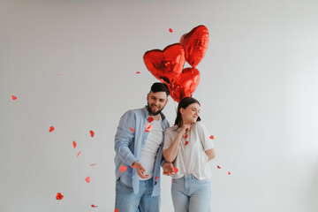 A young millenial man gives red balloons to his sweetheart.