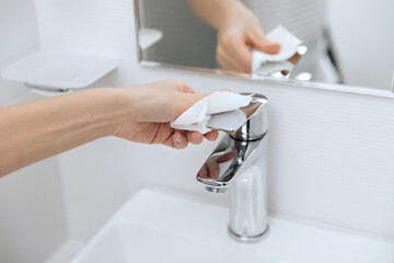 Cleaning the sink faucet with a microfiber cloth. Cleaning the bathroom. Sanitize surfaces prevention in hospital and public spaces against corona virus. Woman hand using wet wipe