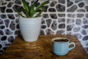 Coffee in cup on wooden table with house plant on blur background, selected focus