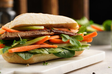Traditional vietnamese banh mi sandwich with sliced smoked tofu, fresh spinach, shredded carrots...