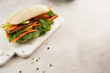 Traditional vietnamese banh mi sandwich with sliced smoked tofu, fresh spinach, shredded carrots...