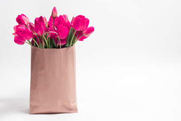 Pink tulips in a craft bag on a white background with a place for text. Congratulations to the holiday birthday, Valentine's Day, anniversary, Mother's Day, Teacher's Day