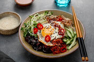 Traditional Korean dish Bibimbap. Bowl with rice, shiitake mushrooms, chicken, cucumber and microgreens and Korean bibimbap sauce. Dark background, copy space for text