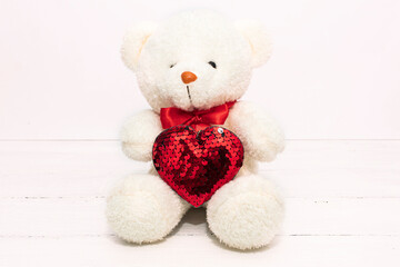 Image of white toy teddy bear sitting on white wooden background with red bow andl heart