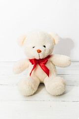Image of white toy teddy bear sitting on white wooden background with red bow