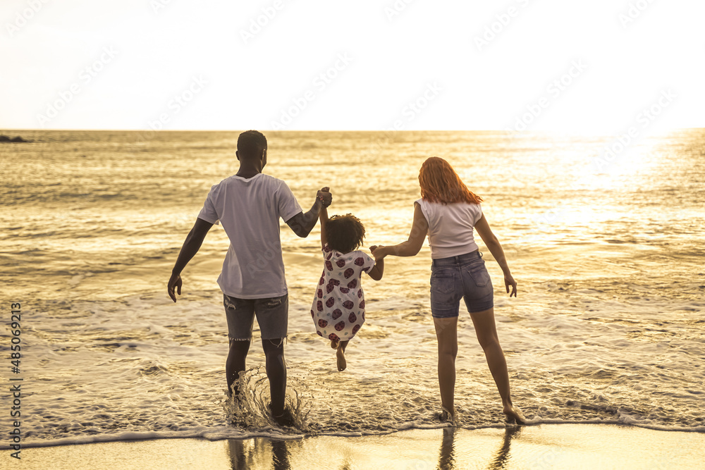 Wall mural multiracial family having fun at the beach. father and mother and daughter playing together outdoor 