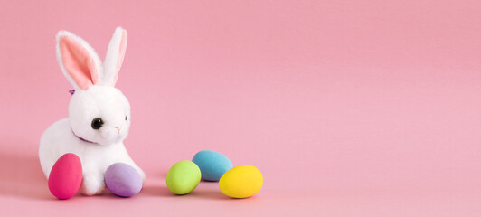 happy easter banner with cute bunny toy and colorful eggs on pink background copy space