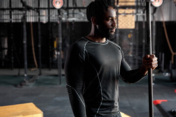 African american athlete male in black sportswear holding barbell bar, preparing for cross fit training, young handsome guy posing at camera, looking at side confidently. Muscular sportsman