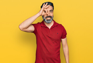 Fototapeta na wymiar Middle aged man with beard wearing casual red t shirt smiling happy doing ok sign with hand on eye looking through fingers