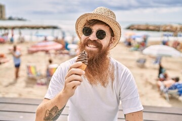 Young redhead tourist man eating ice cream sitting on the bench at the beach.