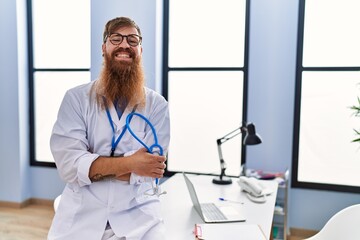 Young redhead man wearing doctor uniform standing with arms crossed gesture at clinic