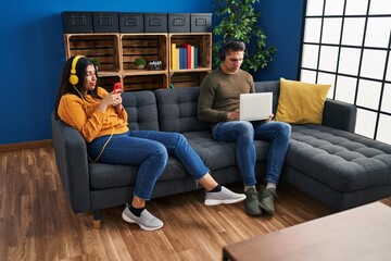 Man and woman couple using laptop and listening to music at home