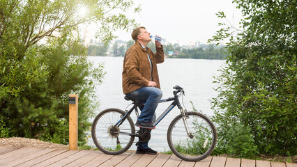 A tired adult man with a bottle of water stopped to drink water during a bike ride.