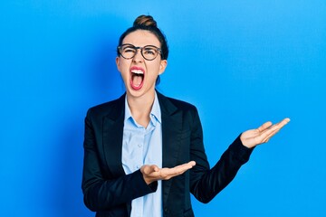 Young hispanic girl presenting with open palms, holding something angry and mad screaming...