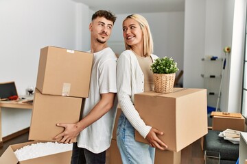 Young caucasian couple smiling happy holding cardboard boxes standing at new home.
