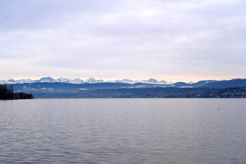 Beautiful scenic landscape with Lake Zurich in the foreground and Swiss Alps in the background on a cloudy winter afternoon. Photo taken February 3rd, 2022, Zurich, Switzerland.